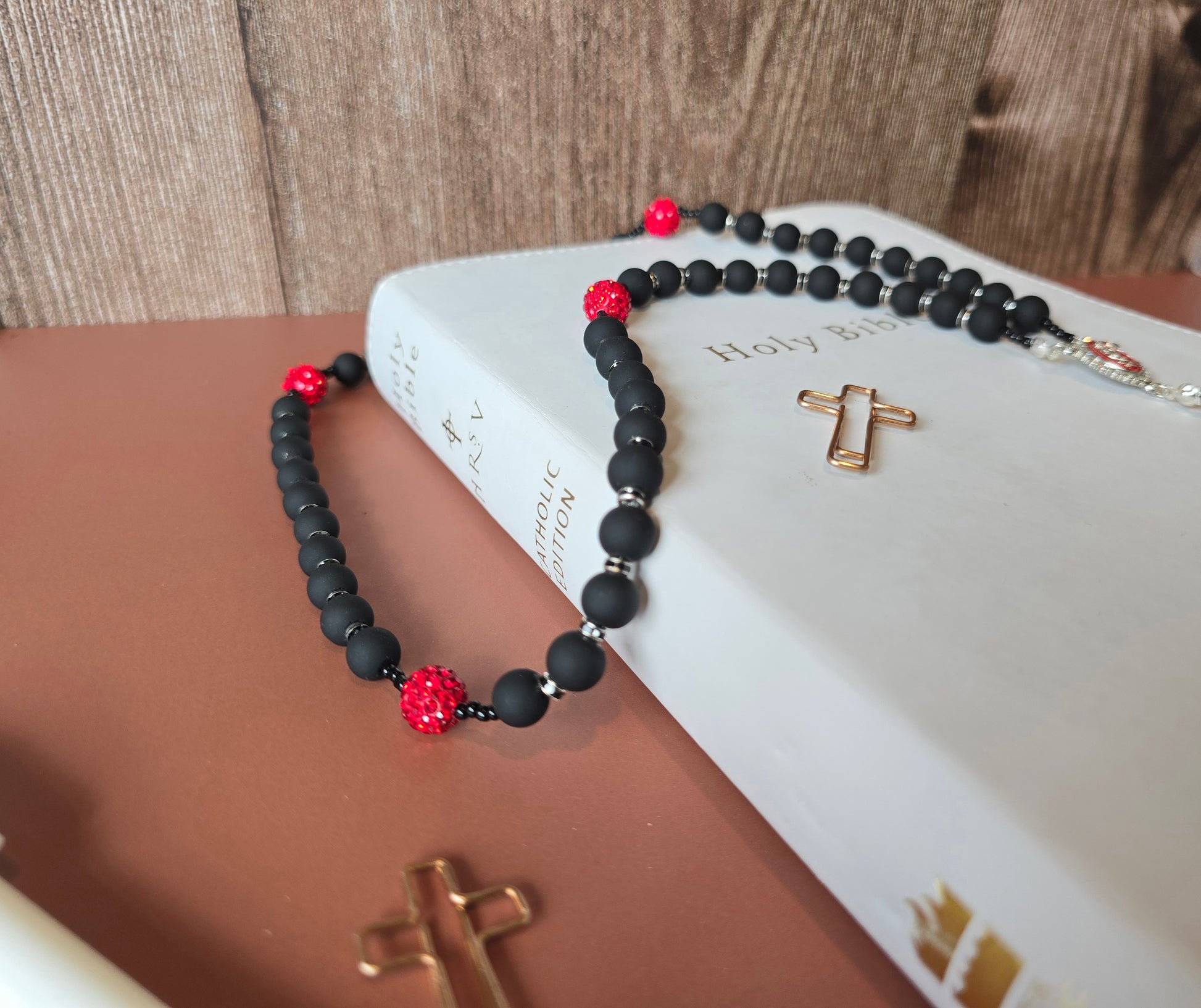 A black rubber coated glass beads and red clay beads with red glass rhinestones laying down on a white bible with a focul point of our black rubber coated glass bead to show their matted texture.